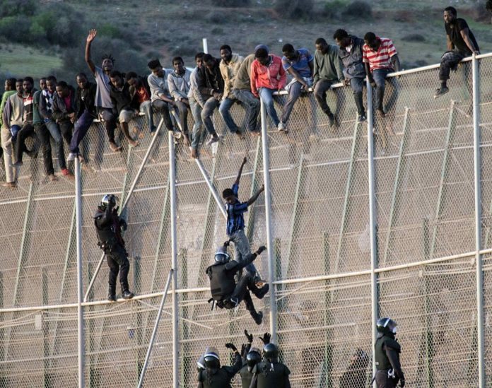 Migrants climb the fence on the border between Melilla and-Morocco